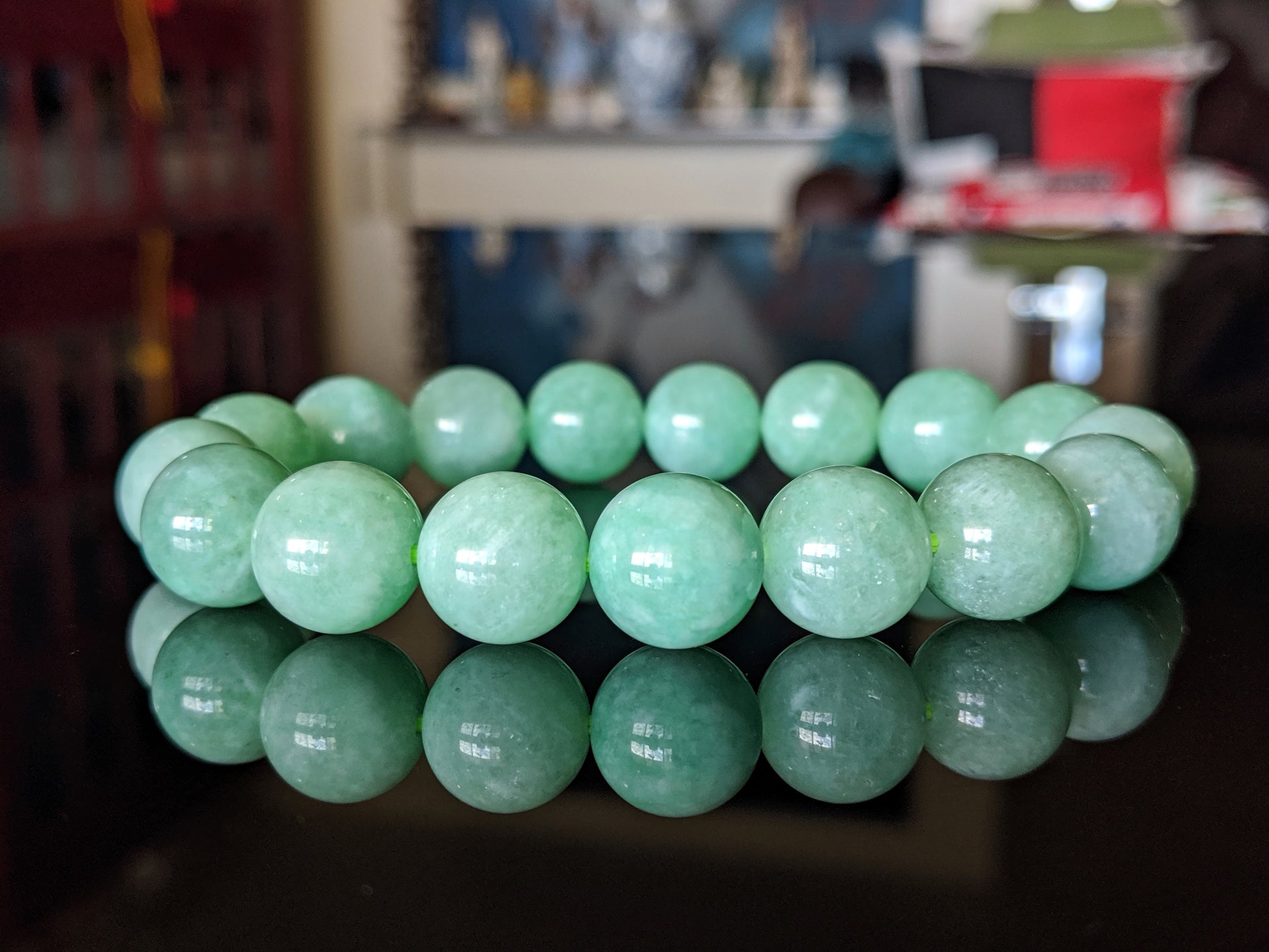 This is the main picture for the Burmese Jade bead bracelet.  The bracelet is displayed on a flat black surface, and its color is a light green. 