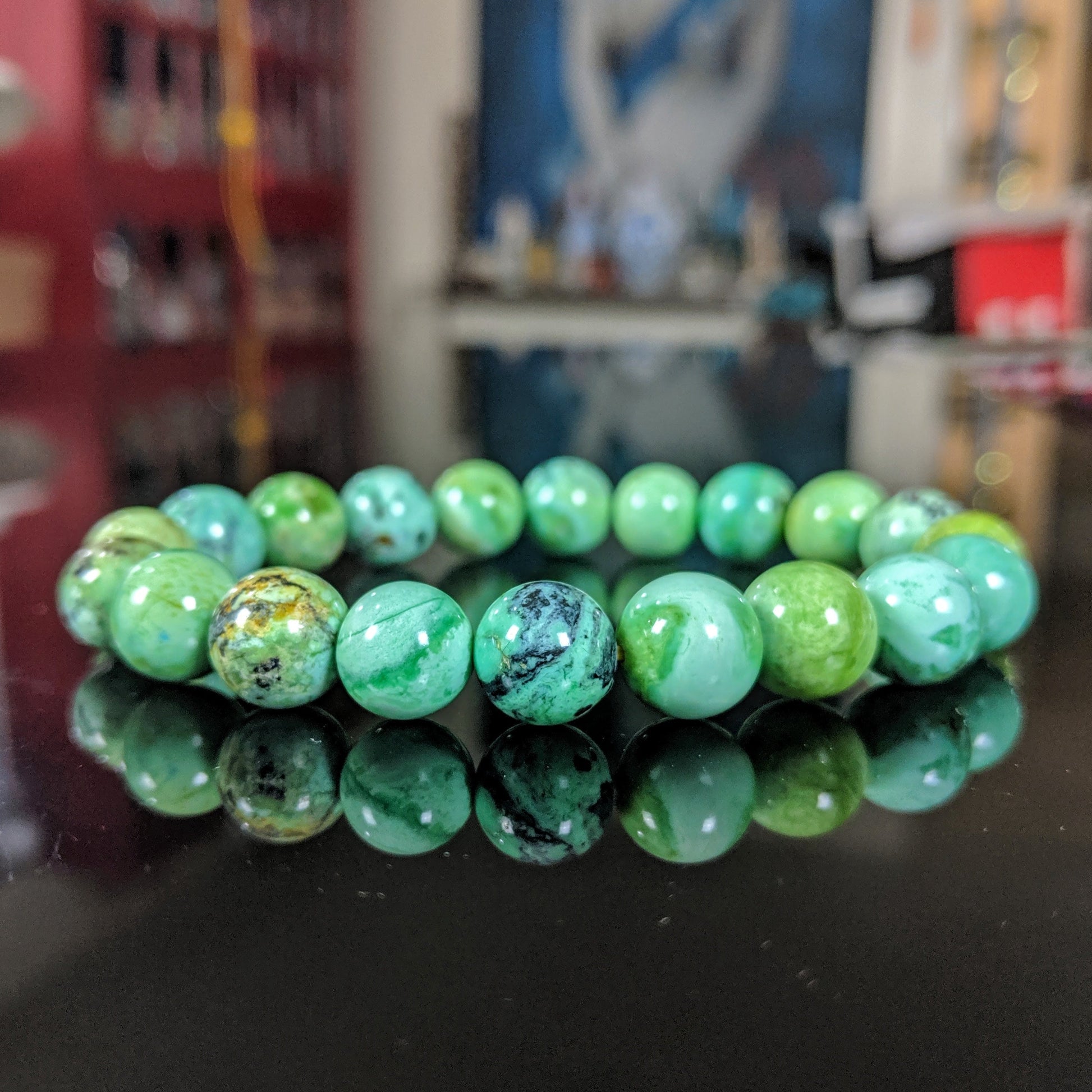 This picture illustrates the Variscite bead bracelet on a black flat surface.  The Variscite material is mainly green with many other hues of colors.  Light, pastel green color, and a vibrant bead bracelet that will make its wearer happy again.