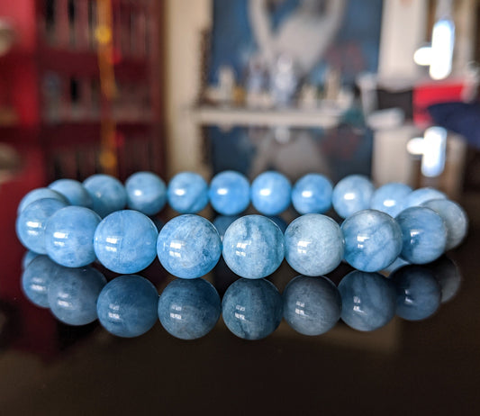 This is the main image for the 2A Aquamarine bead bracelet.  The beads are 10 mm size, strung on durable stretch cord.  The bracelet on this picture is displayed on a flat black surface.  It is a natural light blue. 