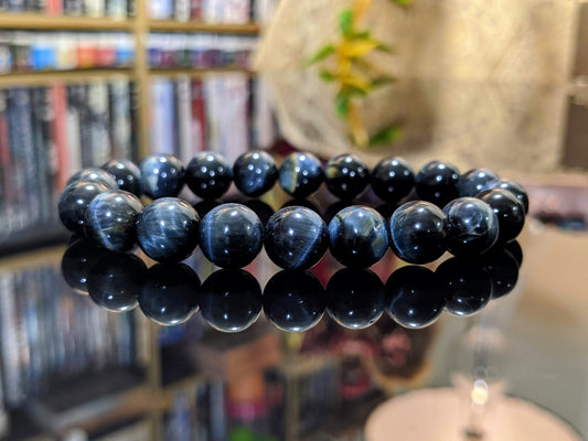 This is the main picture for the Steel Blue Tiger Eye bead bracelet.  The bracelet is displayed on a flat black surface.  Its luster and finish is excellent.  The color is steel blue with high chayotance..  RayonBracelet.com