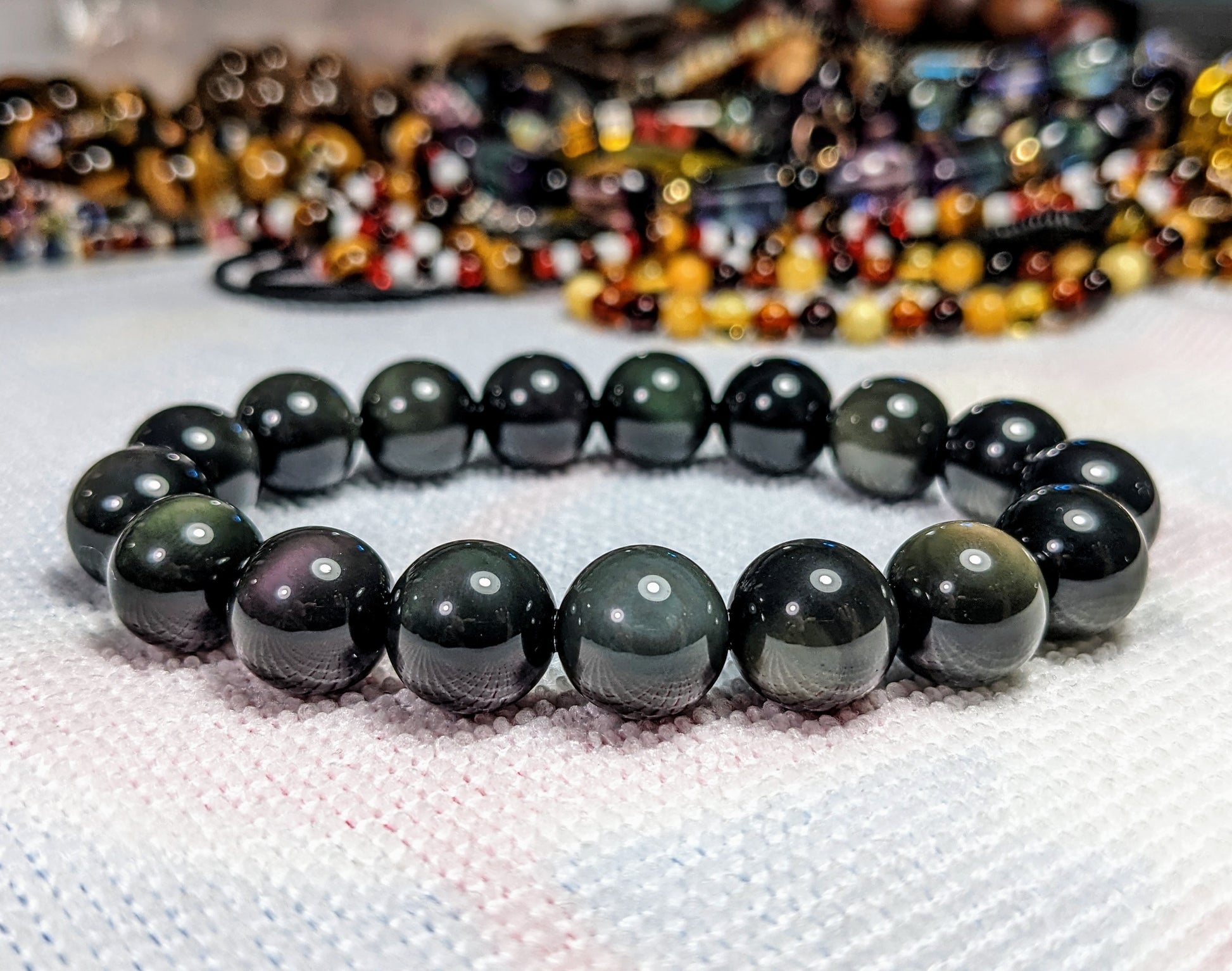 This picture illustrates a high quality green multicolor Obsidian bracelet on a white surface.  The beads are perfectly round and of top quality material. 