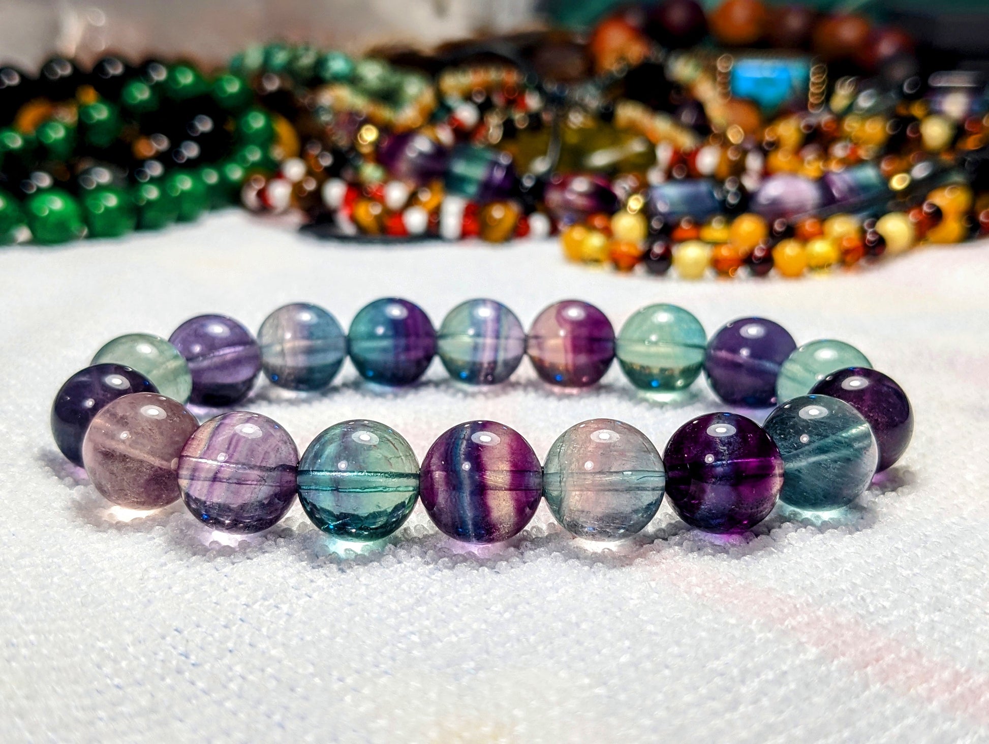 This picture contains a Fluorite bead bracelet on white surface.  It's one of our best seller.  The colors range from purple, clear, blue, green. 