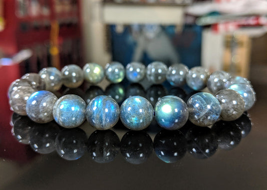 This the main picture for the Labradorite 10mm size bead bracelet.  It is displayed on a flat black surface.  The Labradorite illustrates high chatoyance or shimmer.  Its color vary from a light to dark gray.  It is excellent. 