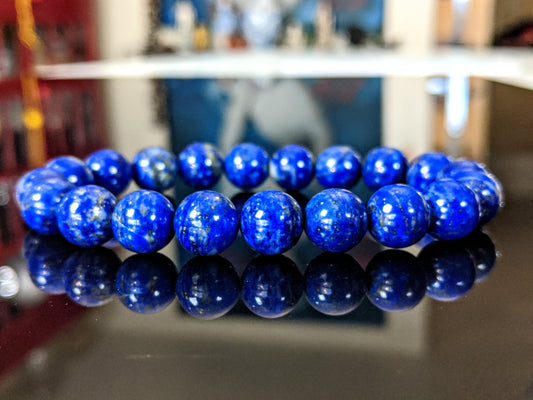 This is the main picture for the A/A- Lapis Lazuli bead bracelet.  This Lapis is  excellent for its metaphysical properties.  It has a good distribution of Calcite as well as Pyrite together with the blue Lapis material.  The item is displayed on a flat black surface . 