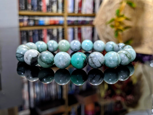 This is the main picture for the 2A+ natural Emerald bead bracelet.  The Emerald is 100% genuine natural with no dyes or treatment.  The Emerald bracelet is displayed on a flat black surface.  The beads have a matte finish, and its color ranges from a mint green to white and black.  