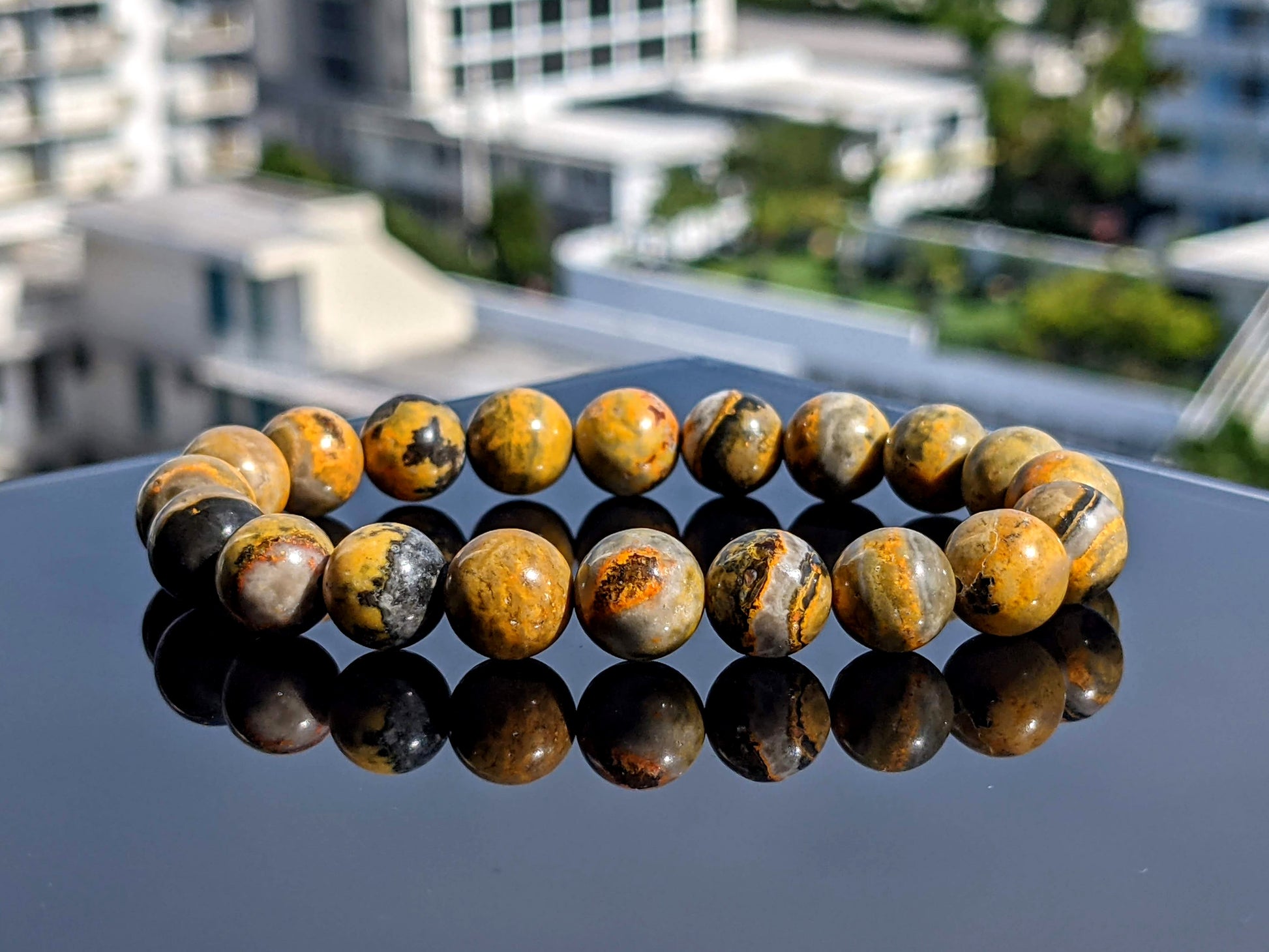 This is the main picture for the Bumble Bee Jasper bead bracelet.  The bracelet is displayed on a flat black surface.  The material is of high quality, and its colors are yellow and black. 