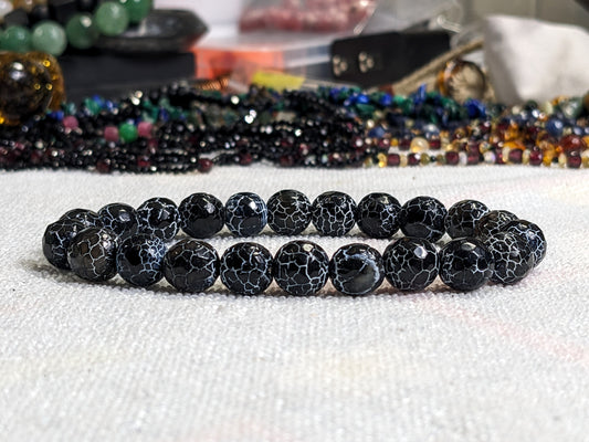 This is the main picture for the White Washed Black Agate bead bracelet on stretch.  The bracelet is displayed on a white surface with an ecclectic colorful backgraound.  The Black Agate has an attractive white crackled finished. 